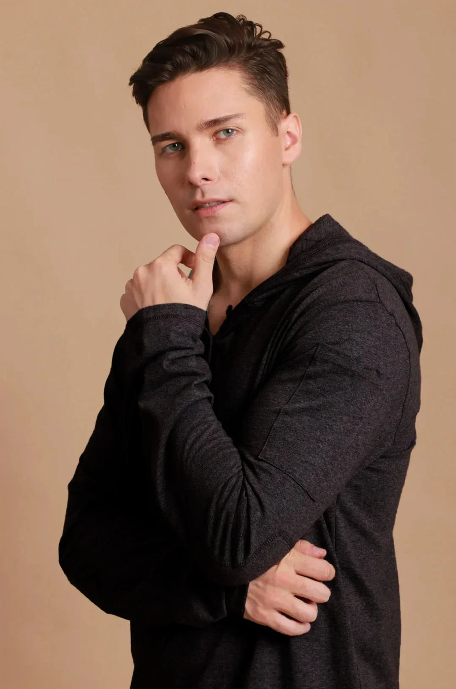 Man wearing a dark long-sleeve organic cotton hoodie against a beige background