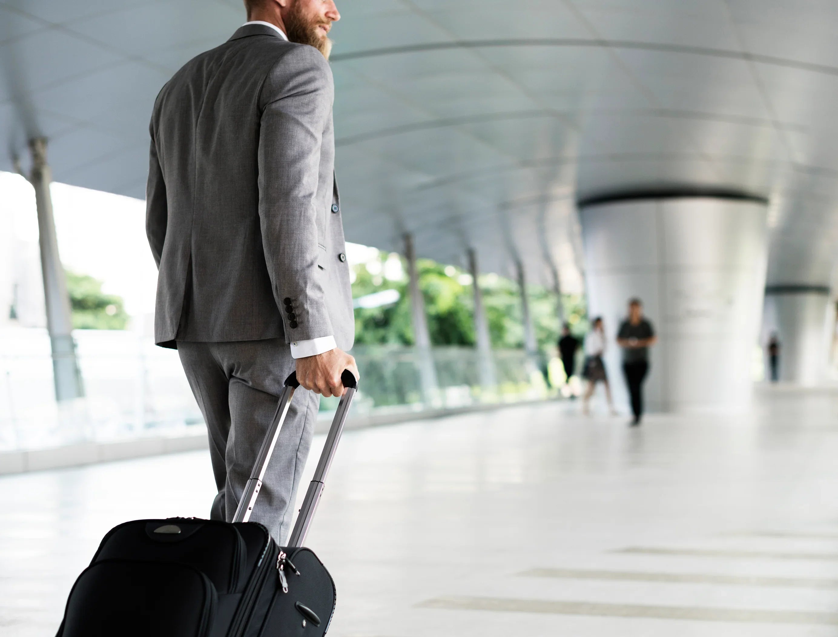 Man in grey suit with suitcase in modern airport walkway, allergy-free travel apparel