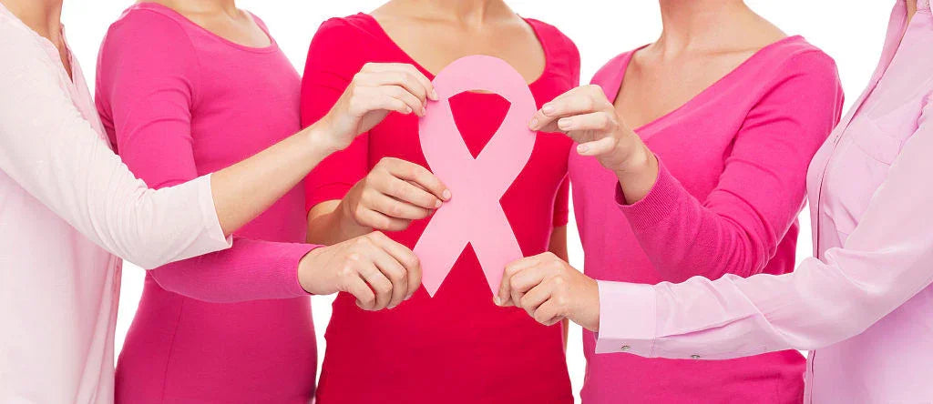 Women in pink tops holding a pink ribbon, symbolizing breast cancer awareness support.