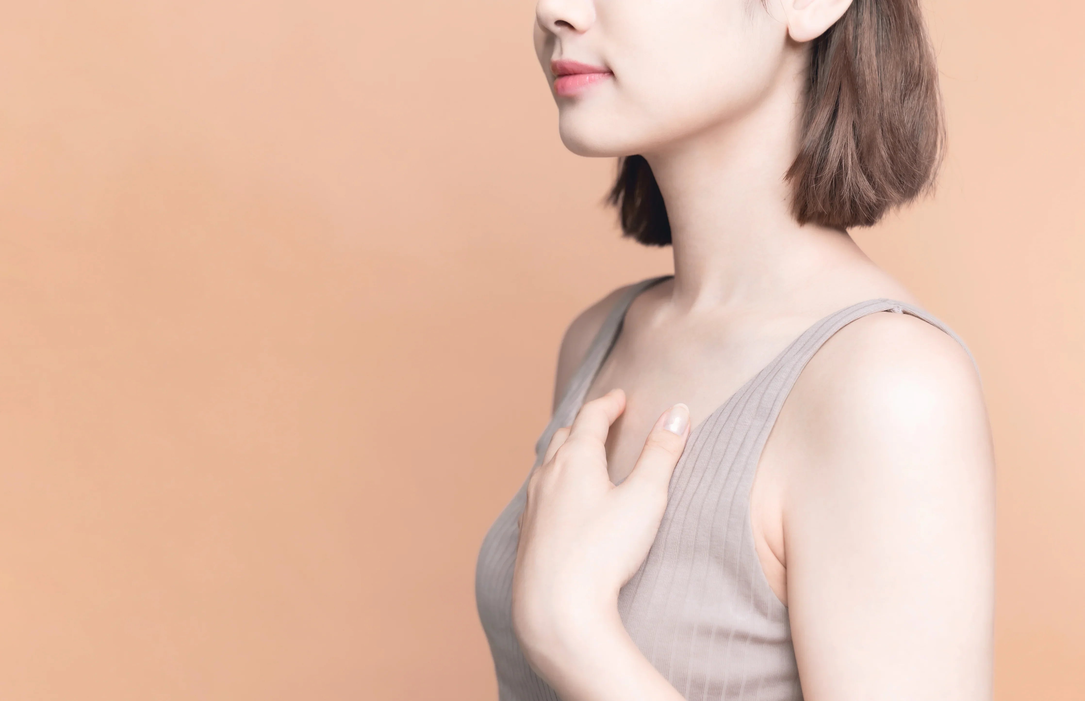 Woman in soft ribbed tank top touching chest, sensitive skin apparel concept, peach background