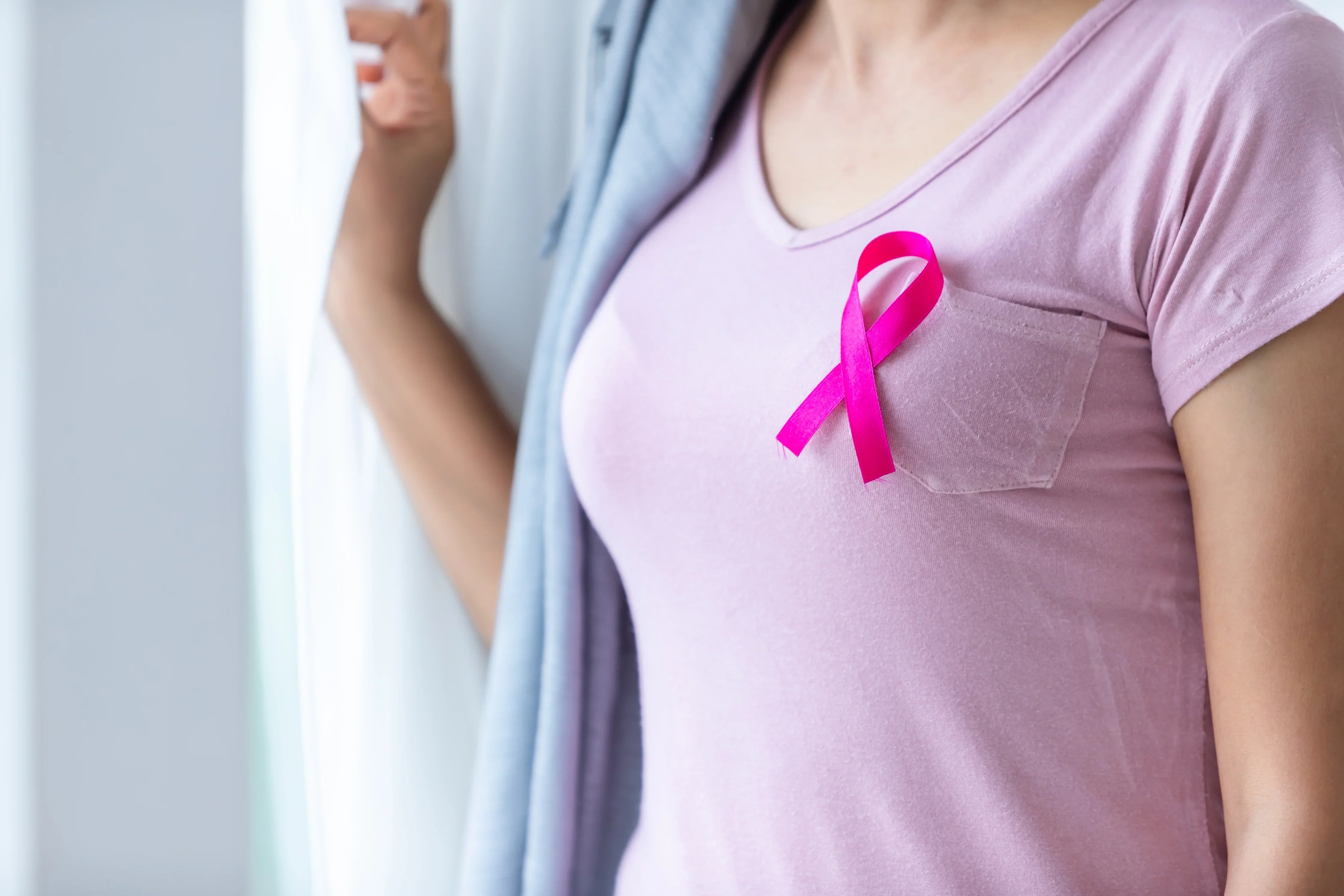 Woman in allergy-free pink Cottonique shirt with breast cancer ribbon by window