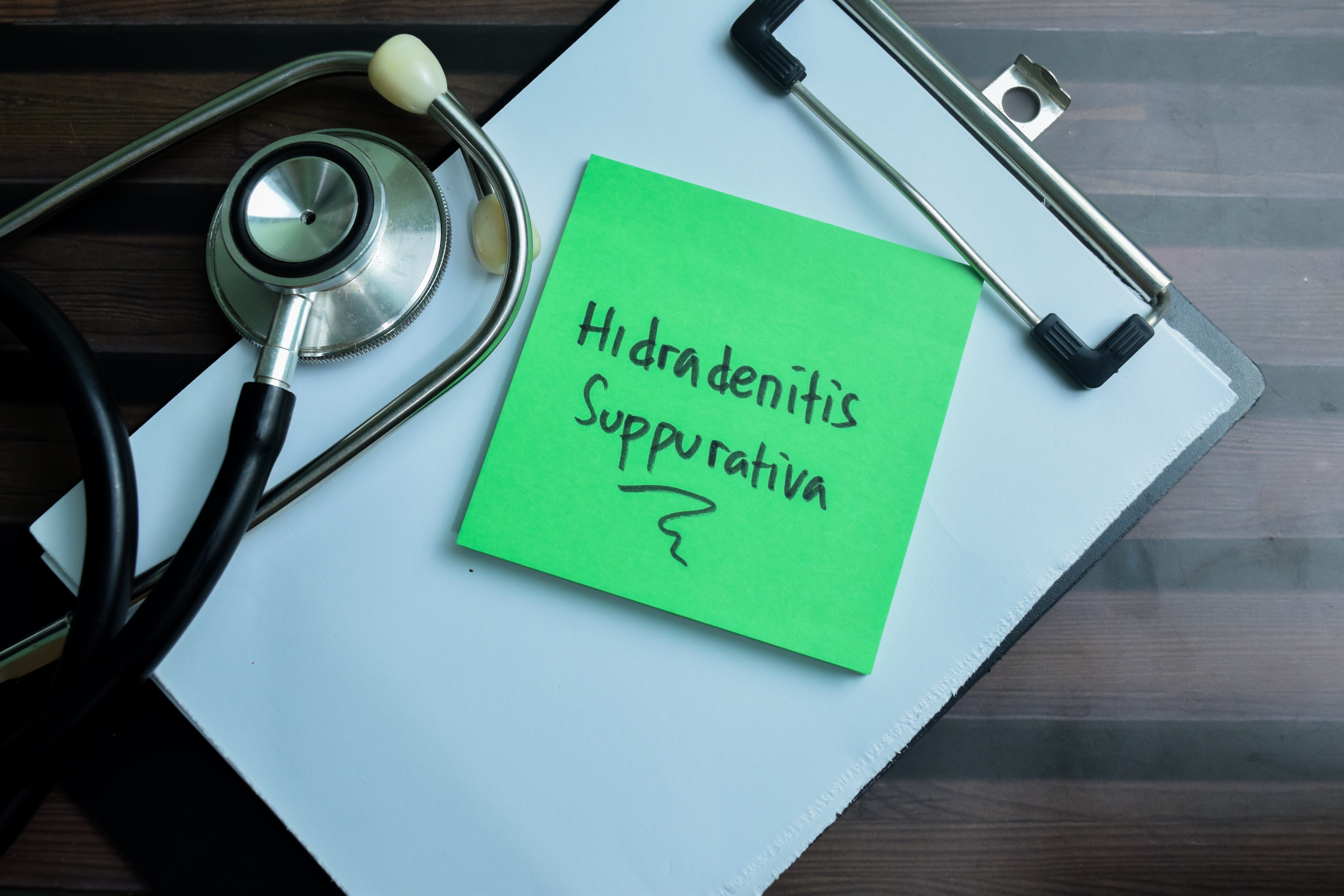A green sticky note on a clipboard with the words Hidradenitis Suppurativa written on it.