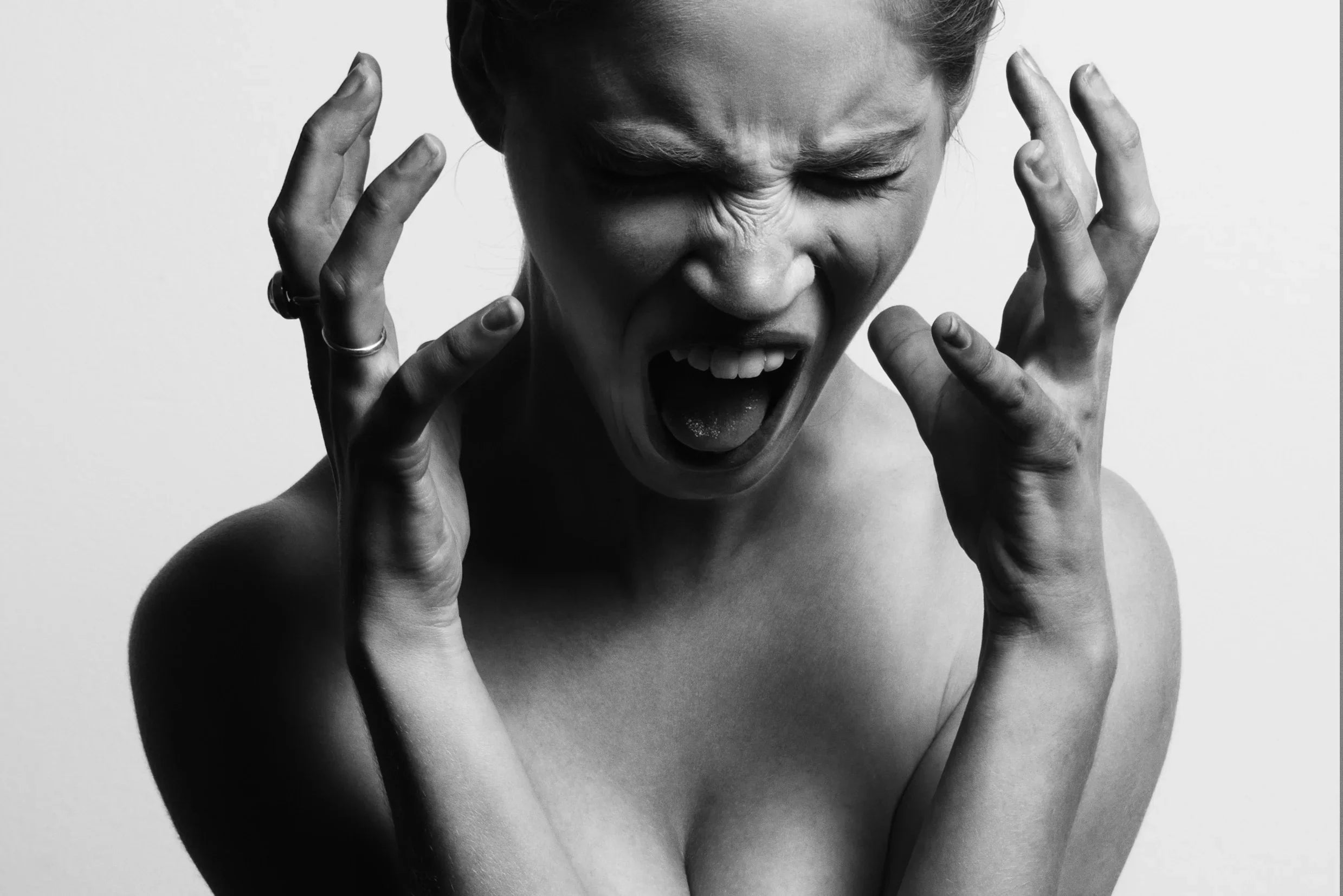 Black and white close-up of a person expressing frustration or discomfort, hands raised, mouth open