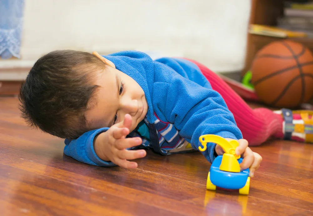 Child in colorful organic cotton clothing playing with toy on wooden floor, basketball in background