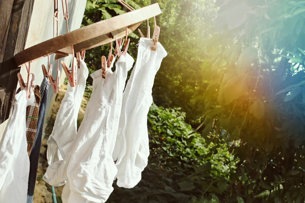 White organic cotton underwear drying on a clothesline outdoors, sunlight and greenery in background.