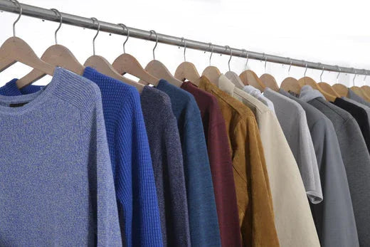 Assorted long-sleeve sweaters and tops in various colors hanging on wooden hangers