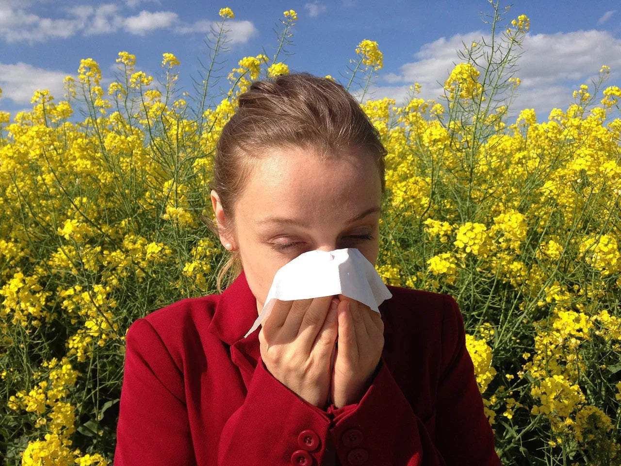 Woman sneezing into tissue near yellow flowers, representing allergy-free apparel need
