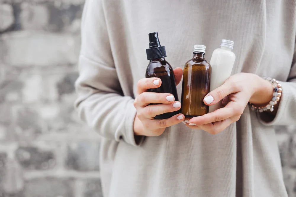 Woman in neutral sweater holding three amber and white skincare bottles for sensitive skin