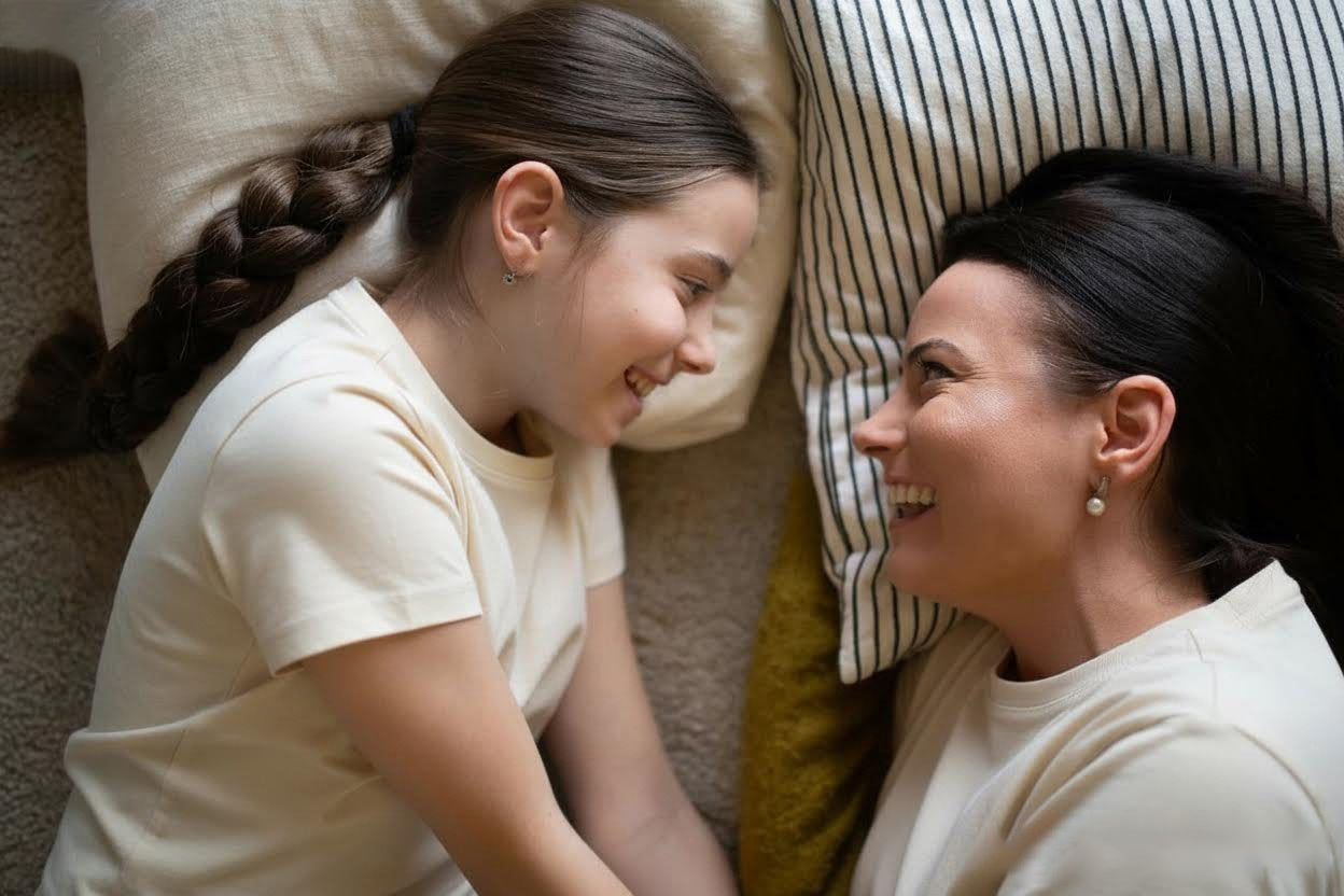 Mother and daughter in soft, organic cotton tees sharing a smile on cozy bedding