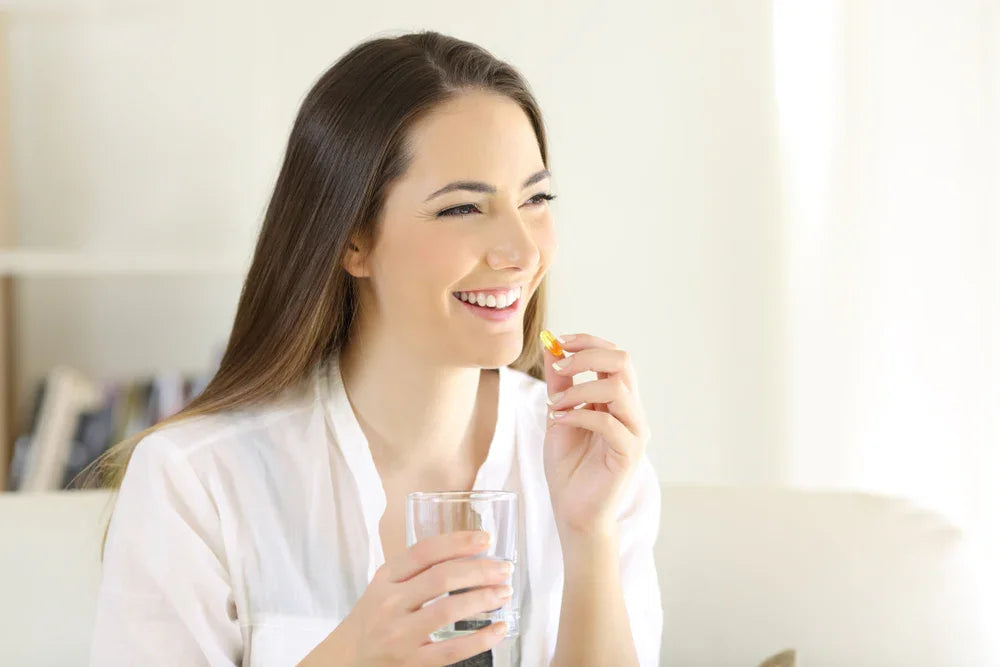 Smiling woman in allergy-free apparel holding a glass of water and supplement indoors