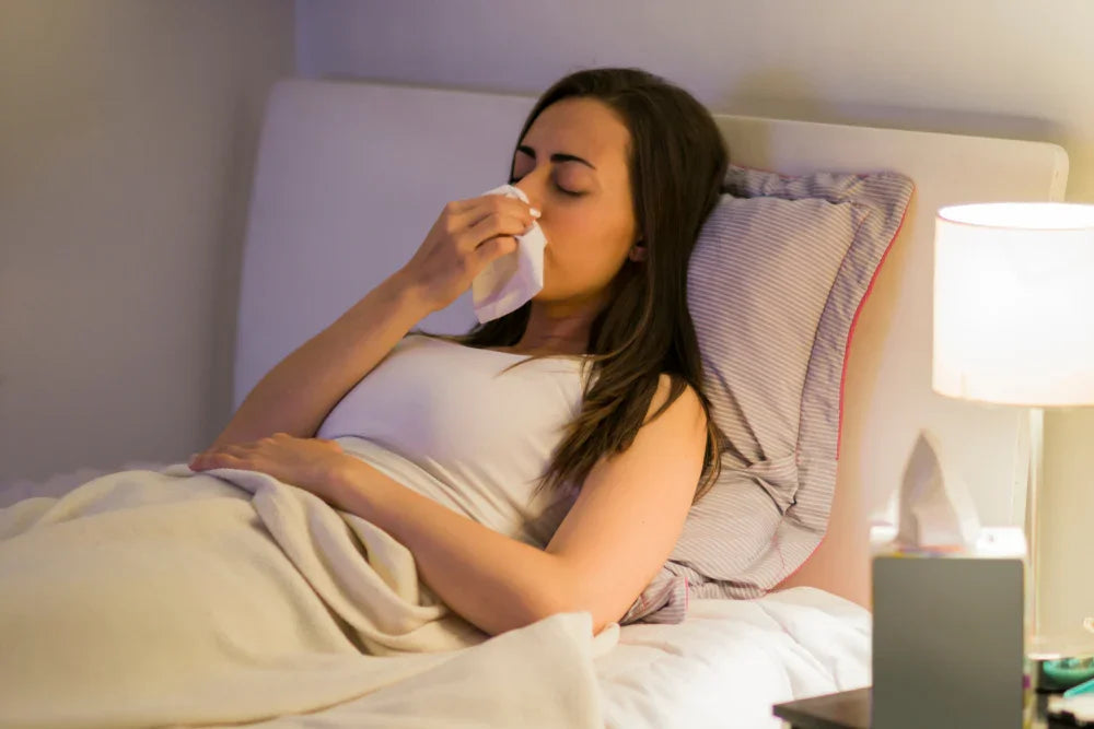 Woman in bed blowing nose, suggesting allergy relief and hypoallergenic cotton bedding