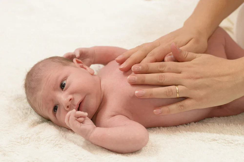 Newborn baby lying on soft fabric while receiving gentle massage, hypoallergenic care concept