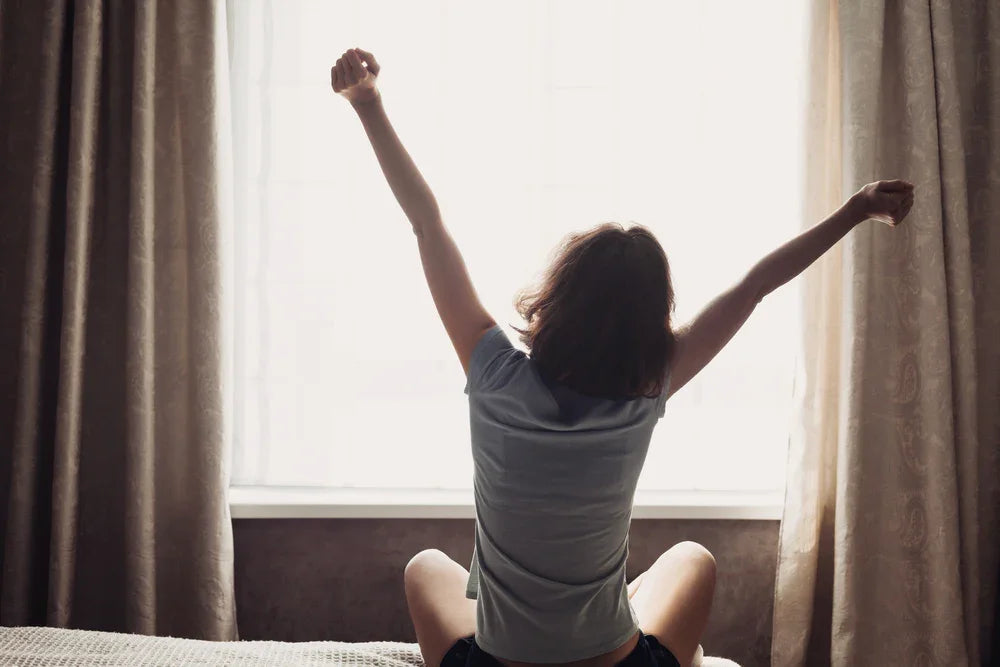 Woman in allergy-free cotton shirt stretching by window, comfortable morning setting