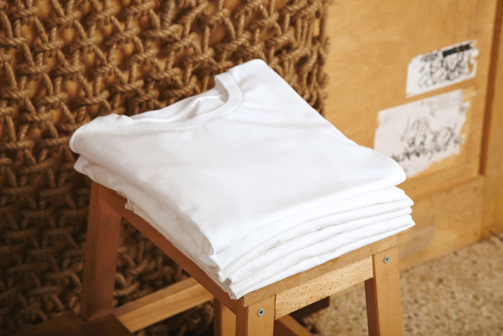 Stack of folded white organic cotton shirts on a wooden stool, allergy-friendly clothing
