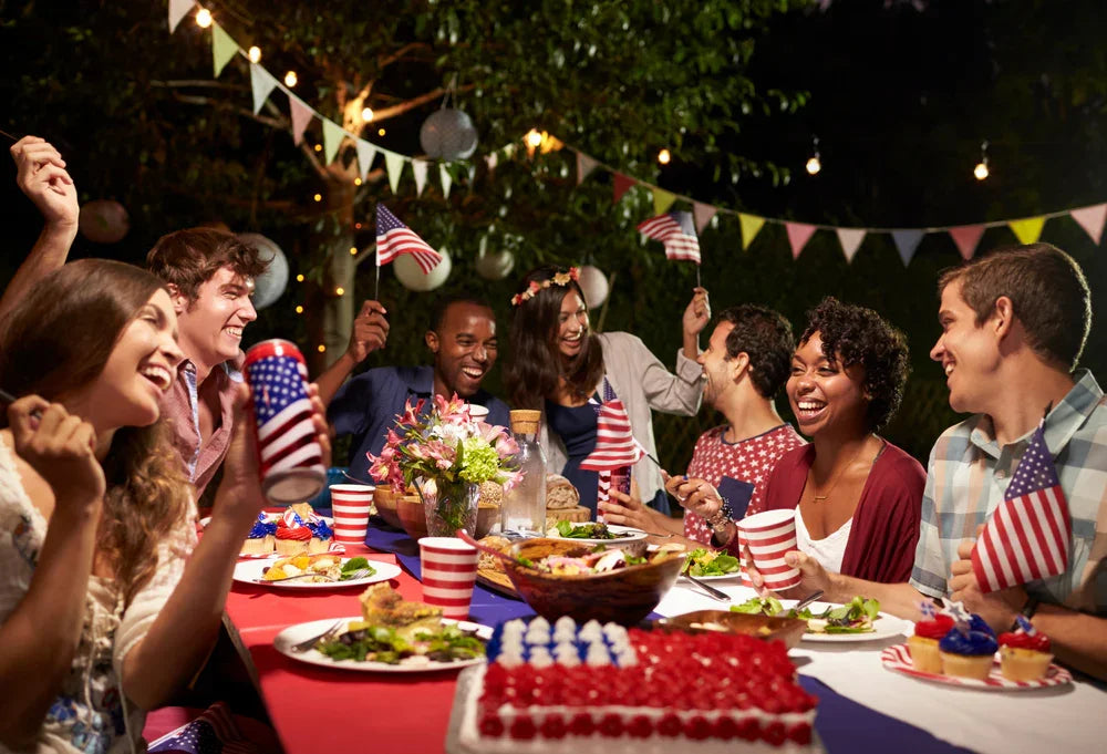 Group of friends at outdoor party with American flags, festive lights, and food