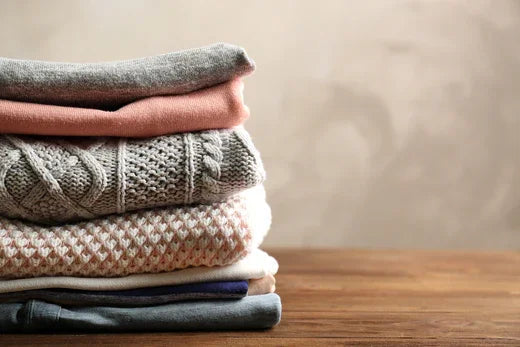 Stack of folded organic cotton sweaters in neutral tones on wooden table for sensitive skin