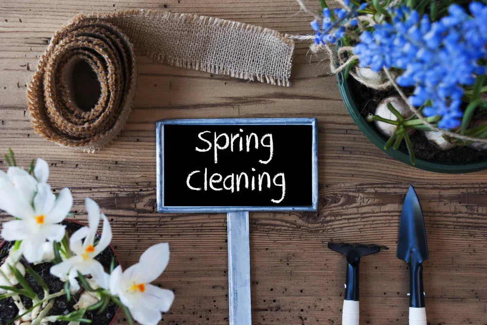 Spring cleaning sign on wood table with gardening tools, potted flowers, and burlap ribbon
