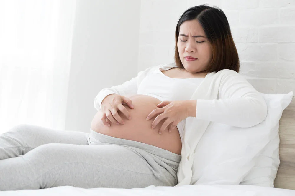 Pregnant woman in comfortable cotton loungewear scratching itchy belly on bed
