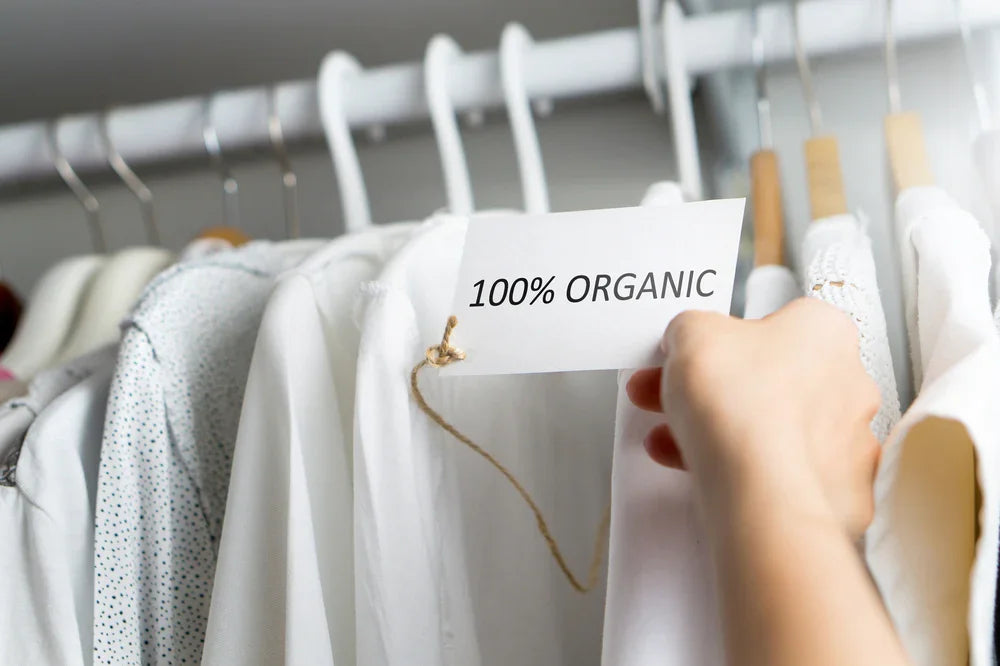 Hand holding 100% organic tag on white cotton clothing for sensitive skin