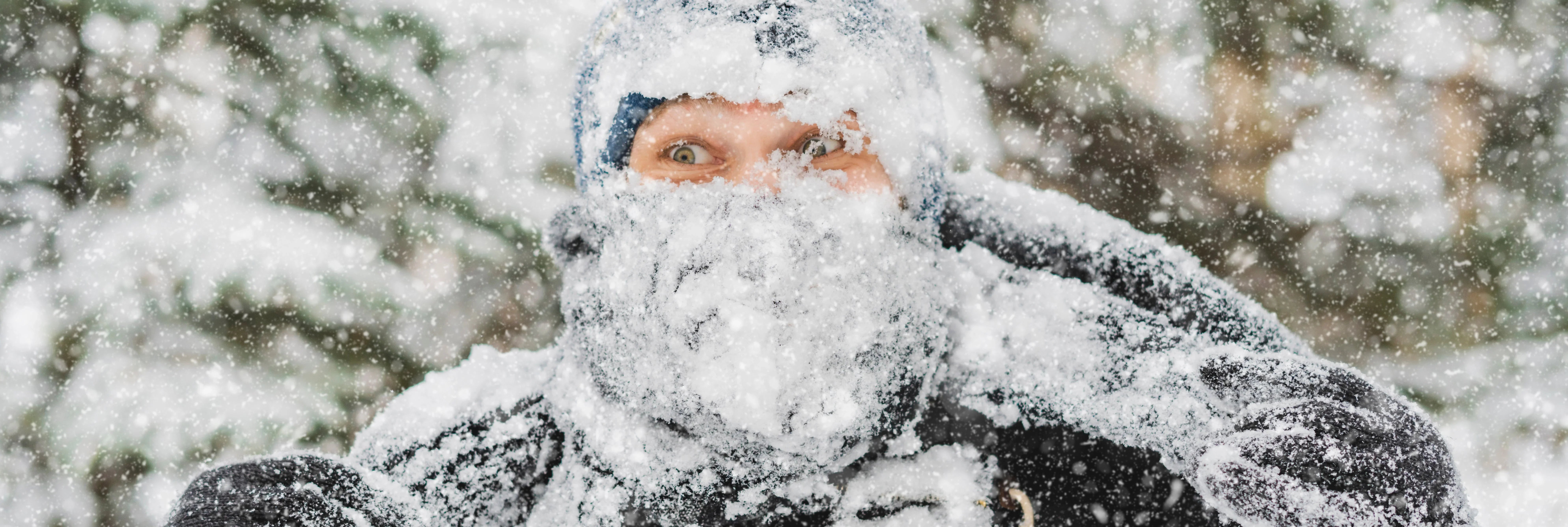 Person outdoors covered in snow during heavy snowfall, wearing winter clothing