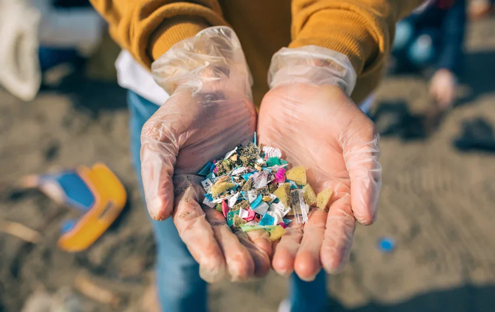 Gloved hands holding microplastics and debris on a beach, allergy-free apparel awareness
