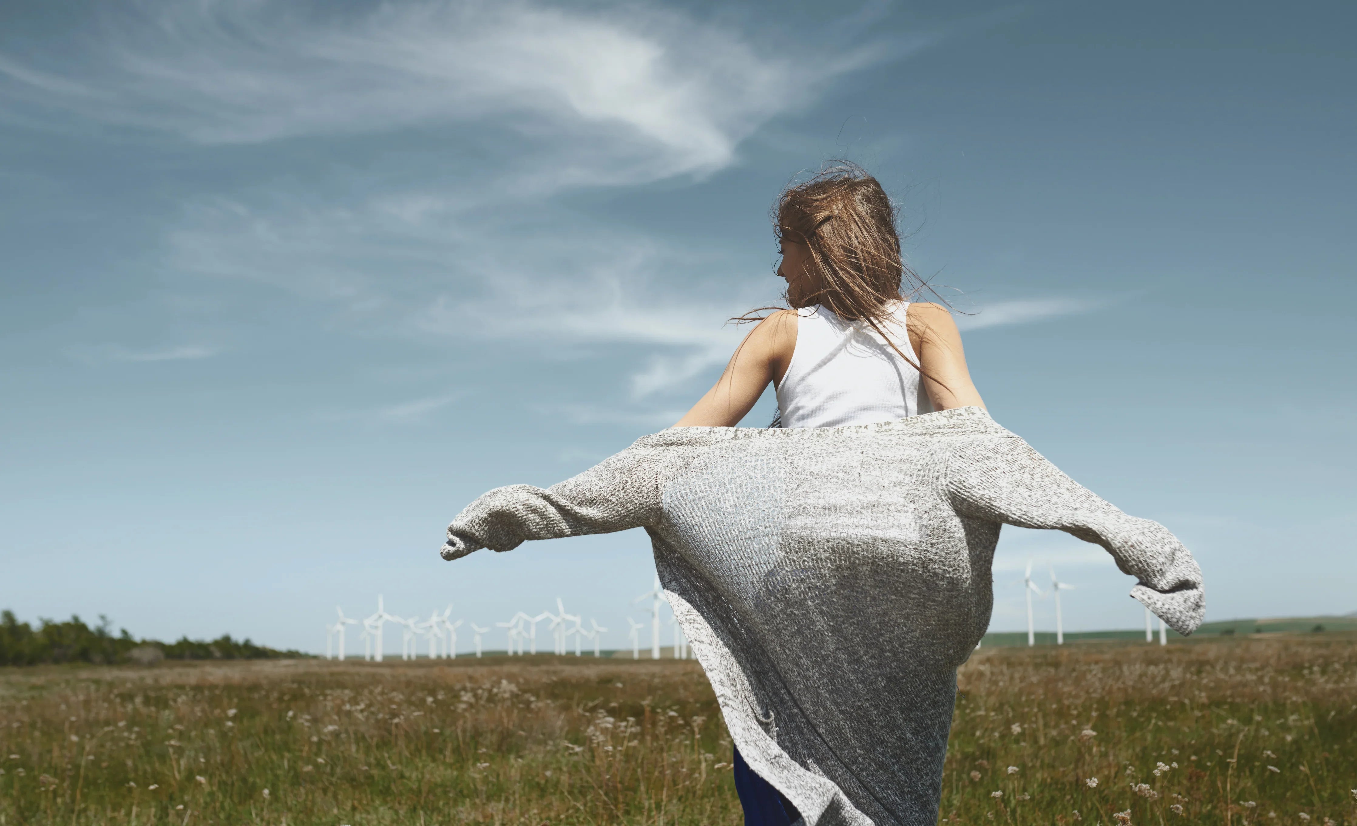 Woman in allergy-free Cottonique apparel enjoying open field with wind turbines and blue sky