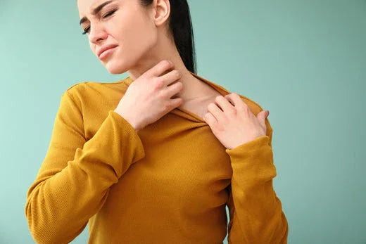 Woman in mustard shirt scratching neck, showing skin allergy discomfort, hypoallergenic apparel concept