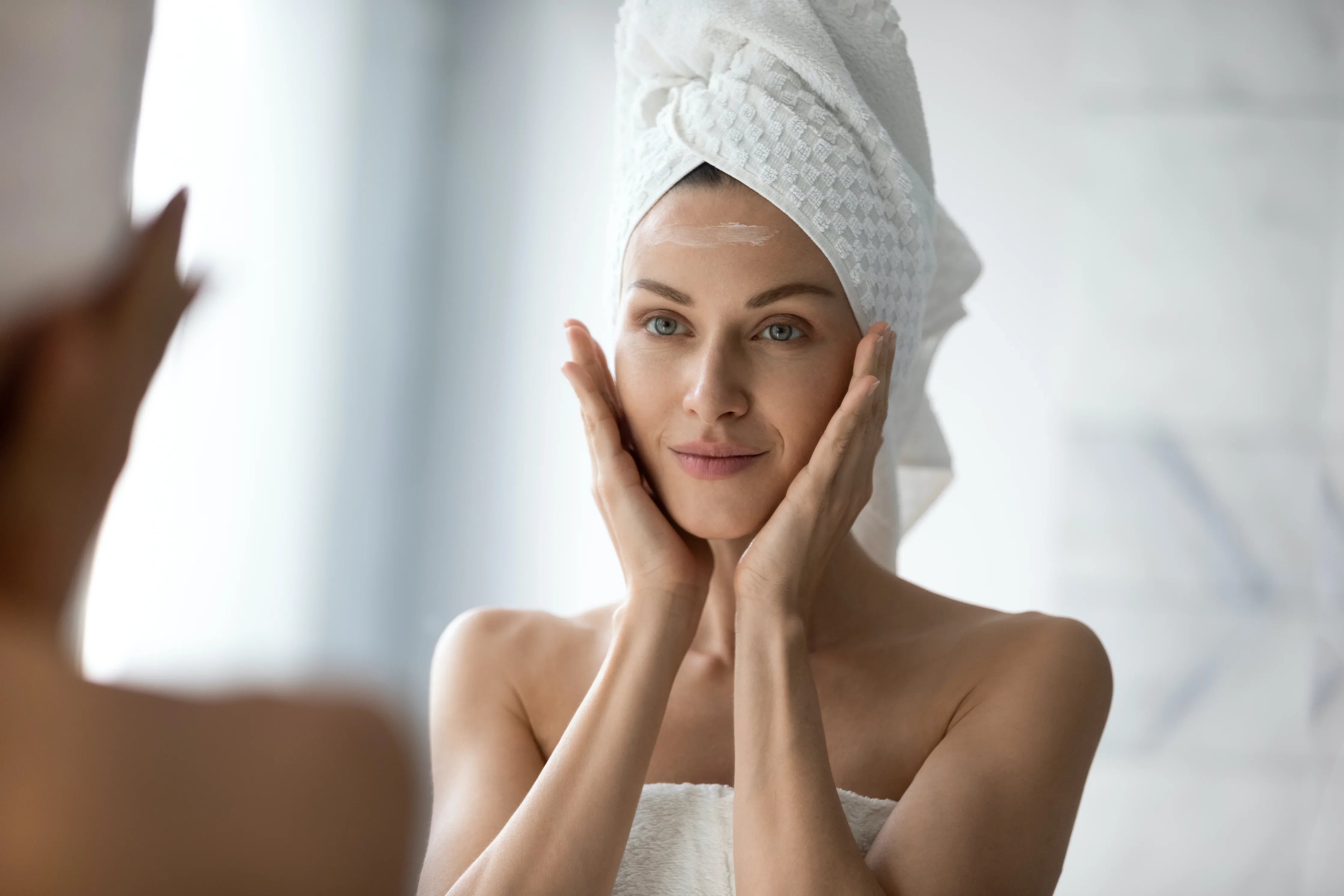 Woman with towel on head touching face in bathroom, natural skincare for sensitive skin
