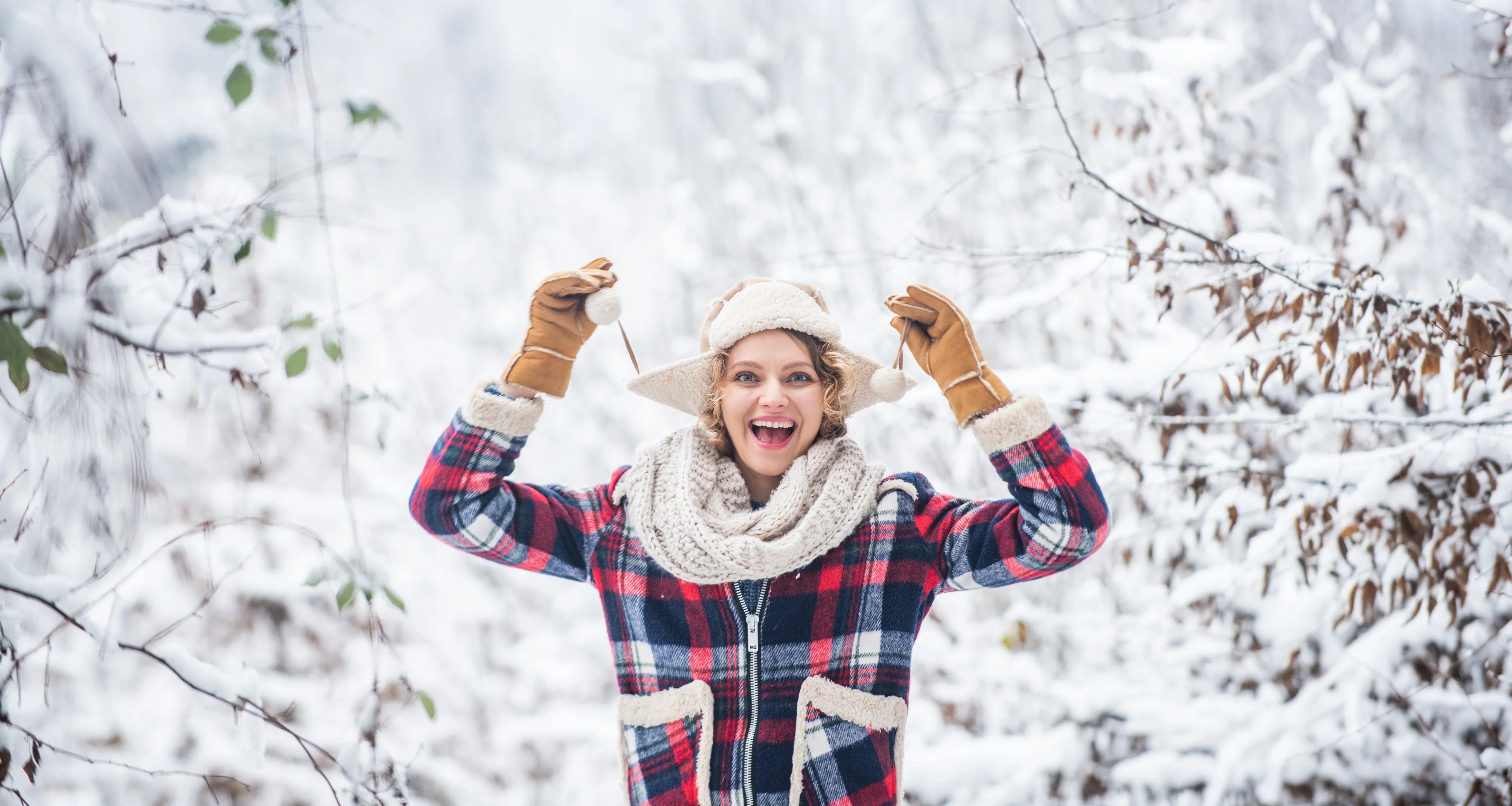 Smiling woman in allergy-free winter apparel and plaid coat outdoors in snowy forest