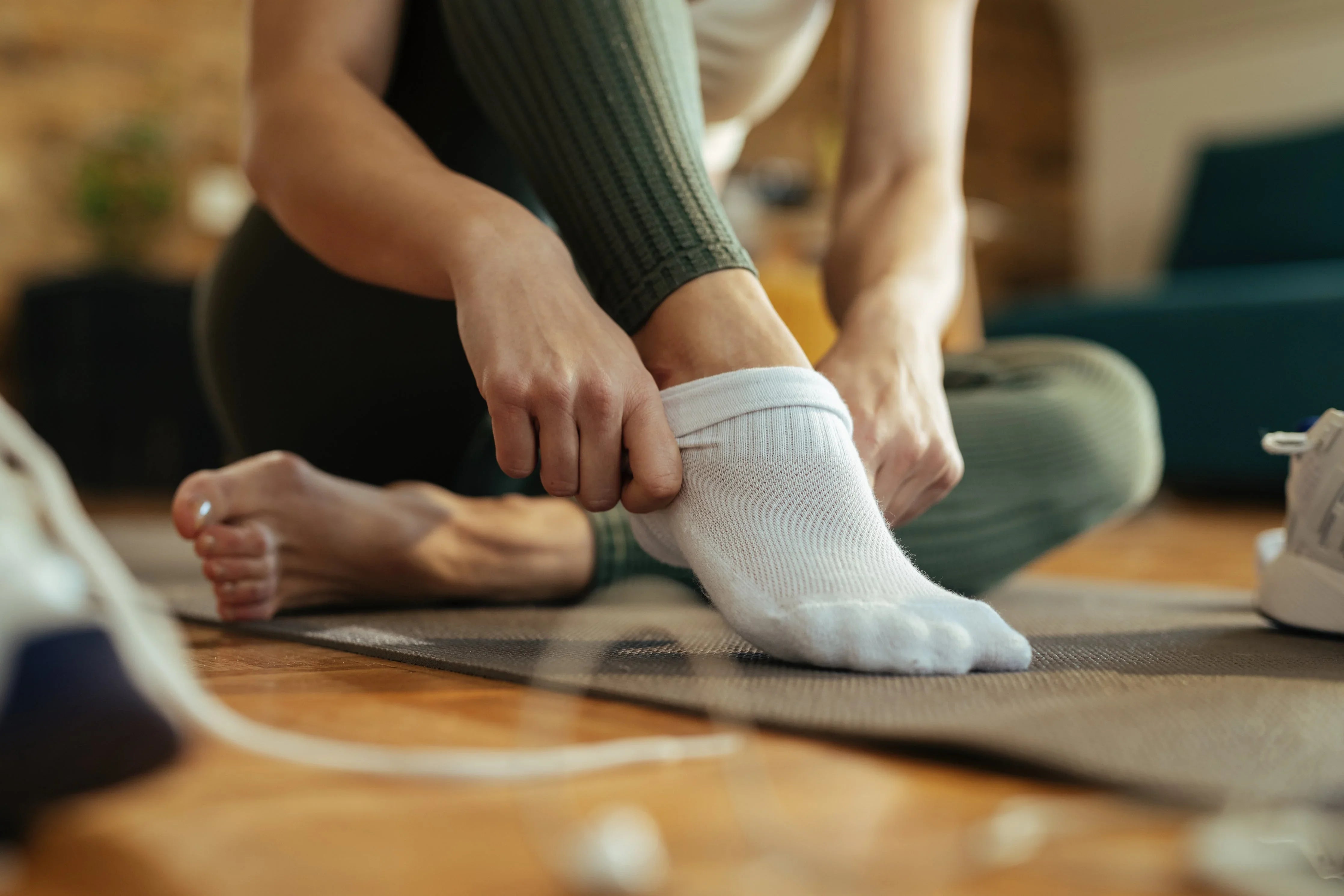 Person putting on white hypoallergenic cotton socks, sitting on yoga mat indoors
