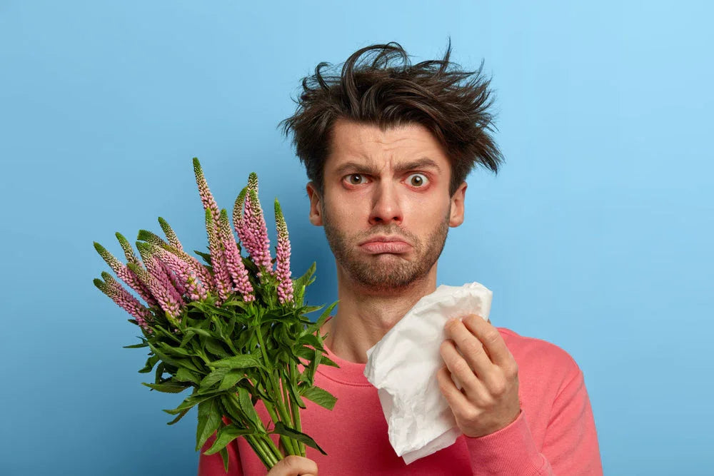 Man with red eyes holding flowers and tissue, showing allergy symptoms
