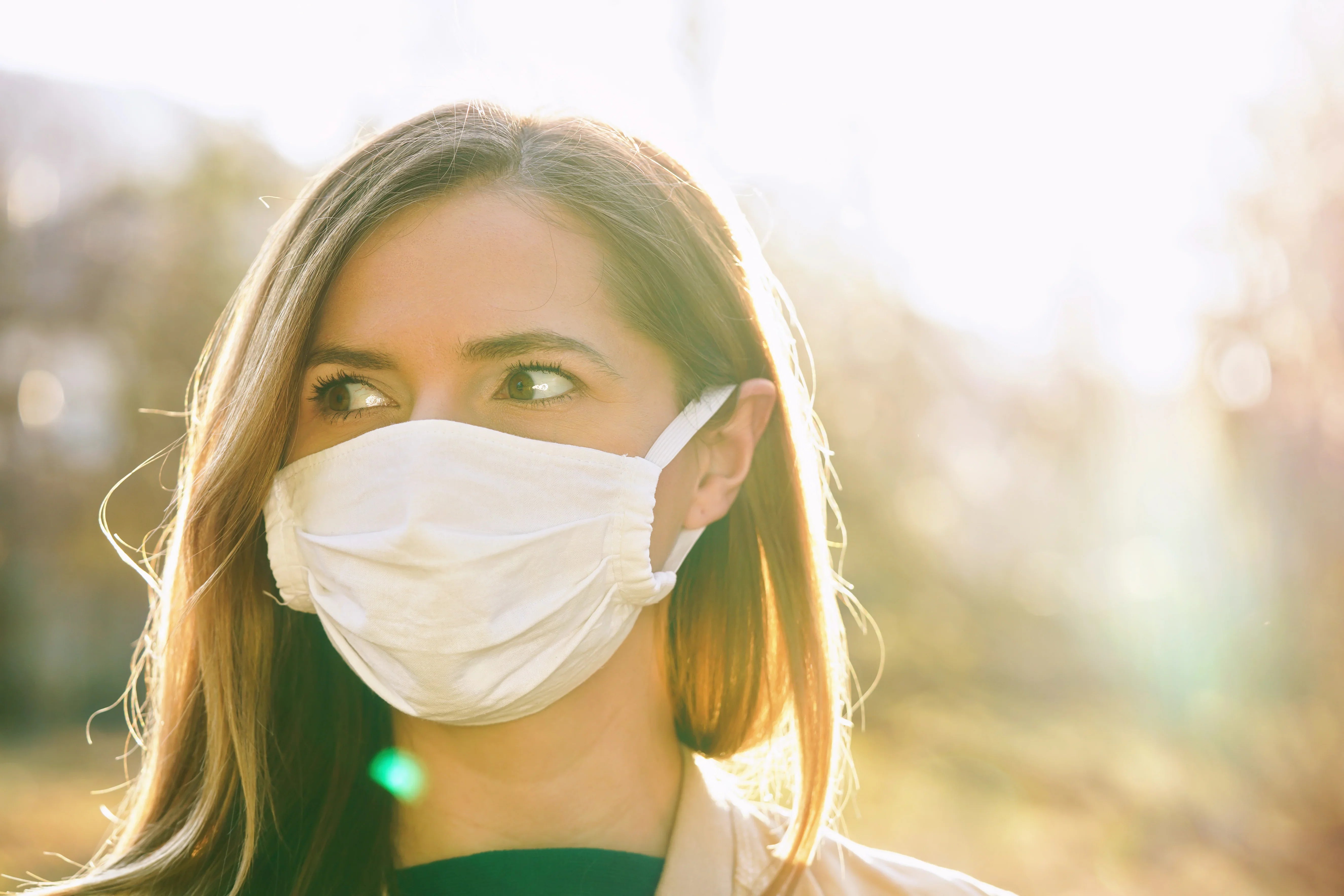 Woman wearing white organic cotton face mask outdoors in sunlight