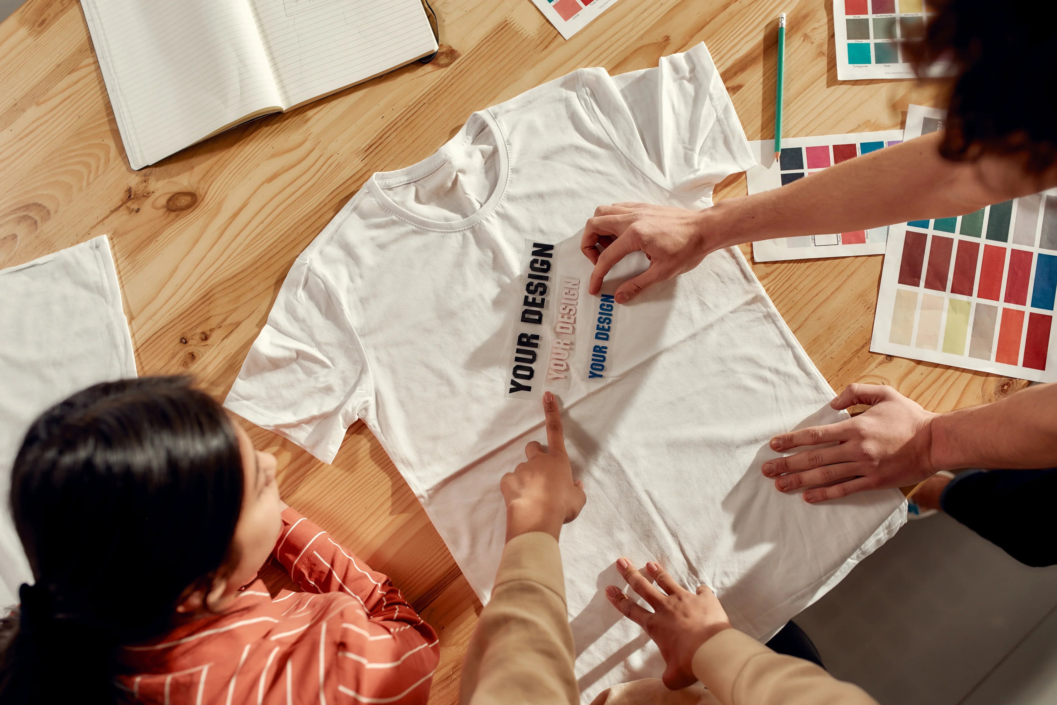 People designing a white cotton t-shirt with custom text samples on a wooden table
