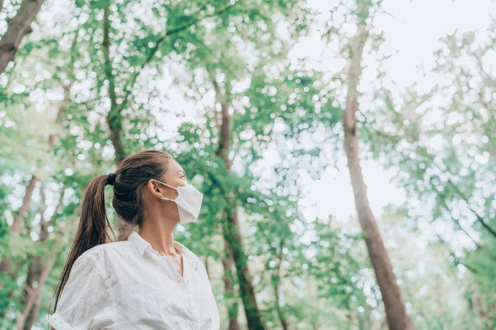 Woman wearing a white cotton face mask and shirt outdoors in a green forest