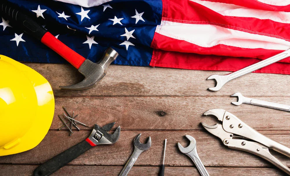 Yellow hard hat, wrench, hammer, pliers, and USA flag on wooden table, construction theme.