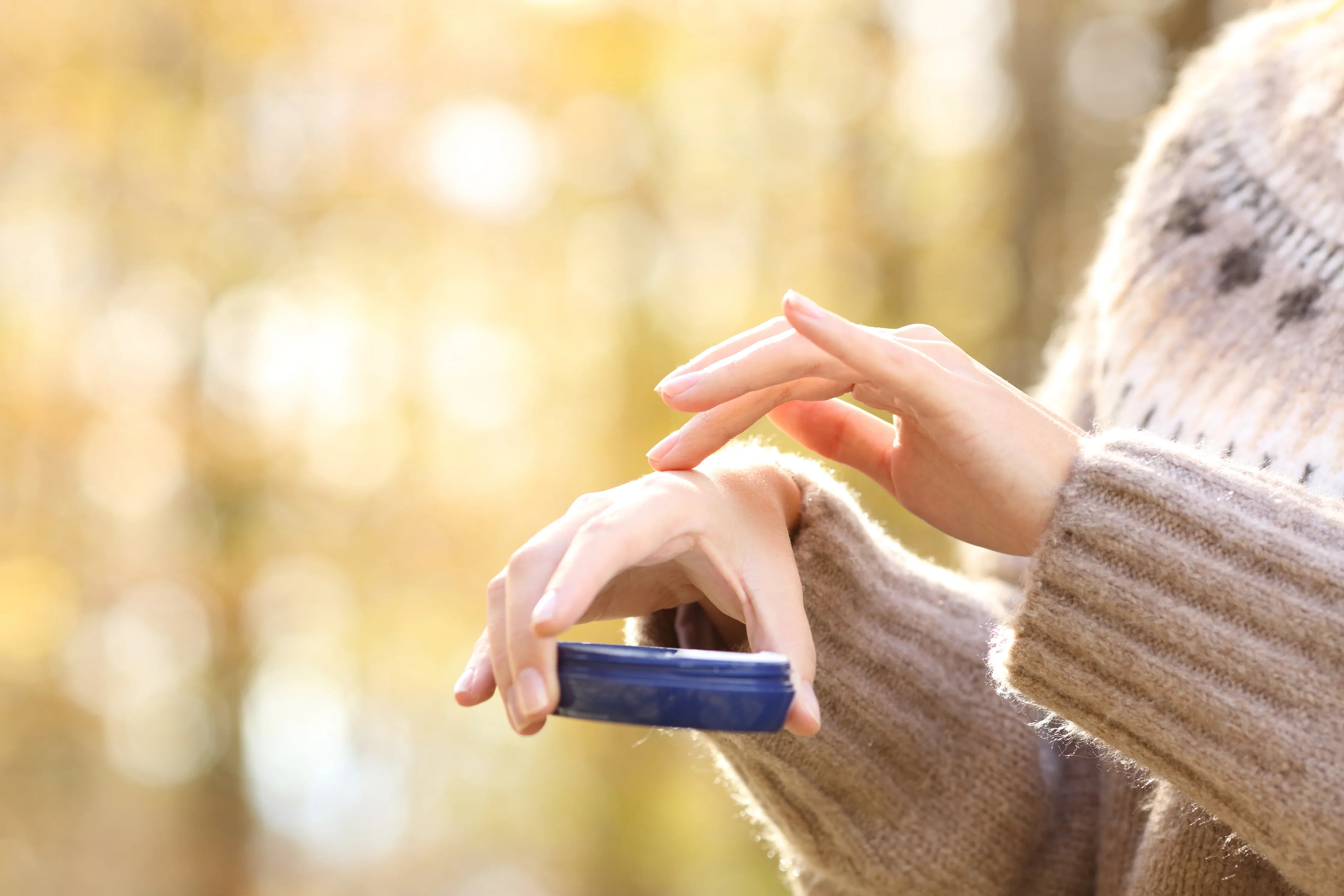 Person in a hypoallergenic sweater applying cream to hands outdoors
