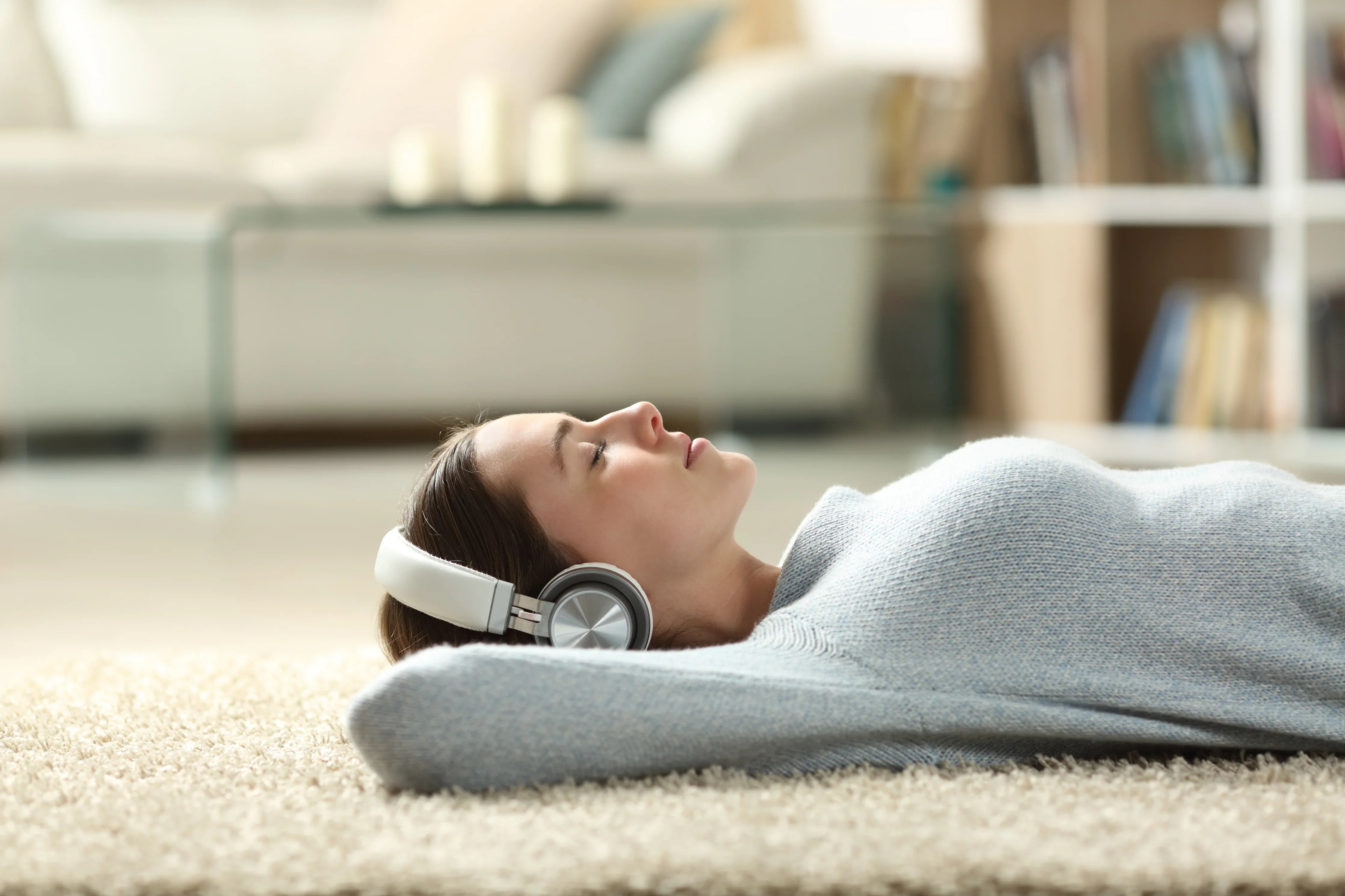 Woman relaxing on carpet in allergy-free cotton sweater, wearing headphones, cozy home setting