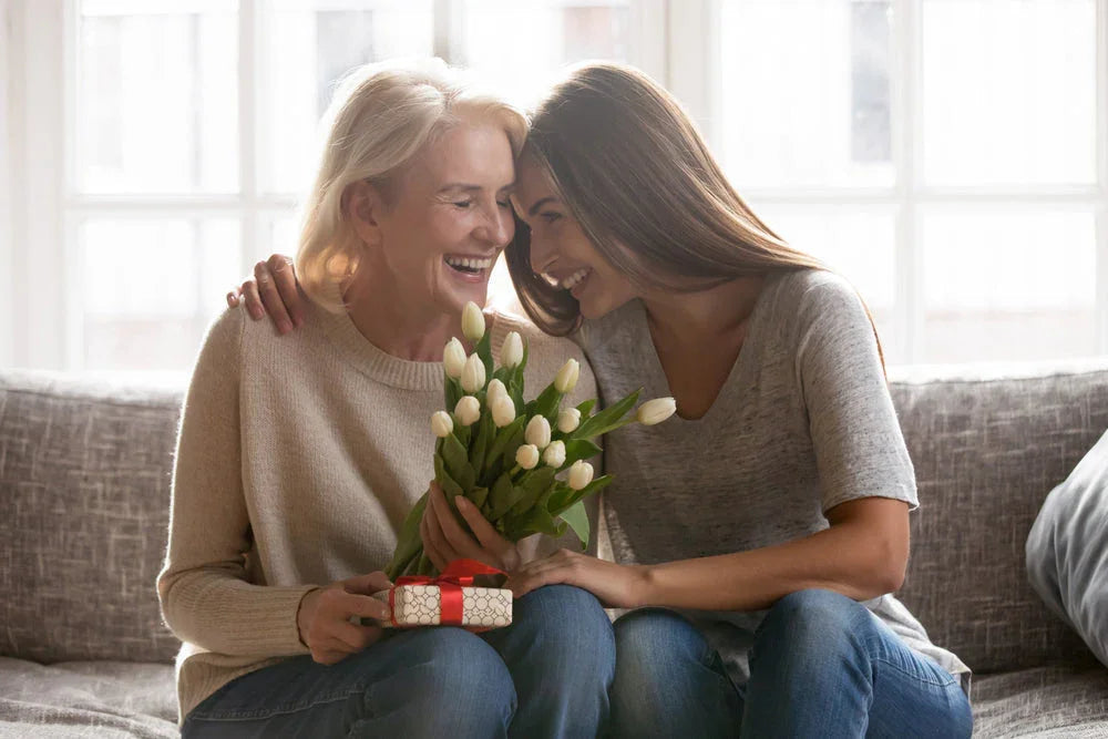 Happy mother and daughter on sofa with white tulips and a small gift, wearing casual cotton tops