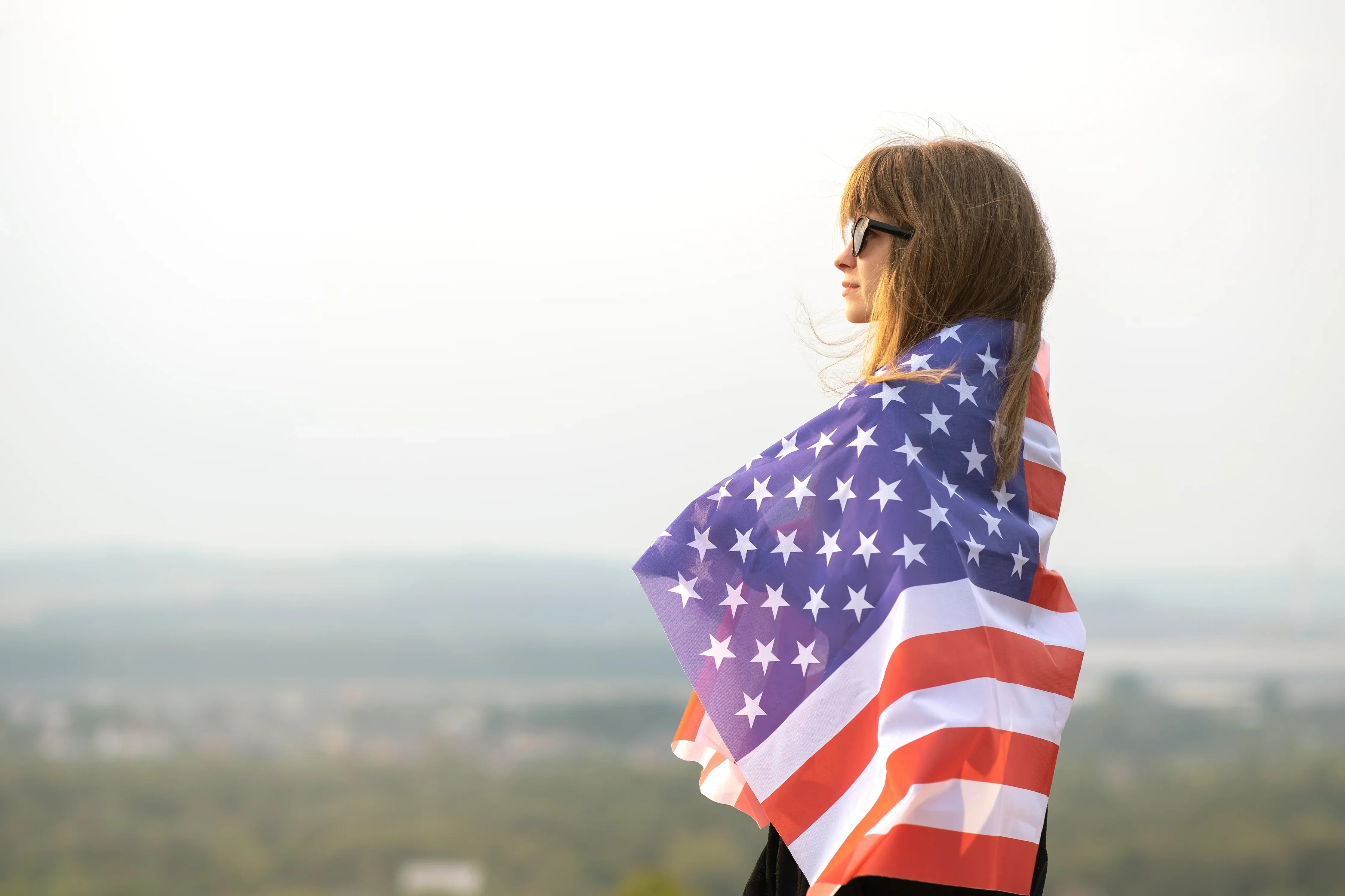 Woman outdoors wearing sunglasses and draped in an American flag, allergy-free cotton apparel