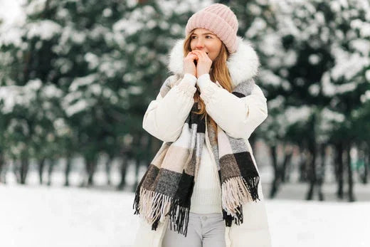 Woman in winter coat, knit hat, and striped scarf standing in snowy outdoor setting