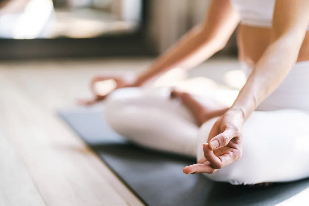 Woman in white organic cotton yoga wear meditating on yoga mat indoors