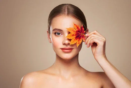 Woman with bare shoulders holding autumn leaf near face, clear skin, sensitive skin care