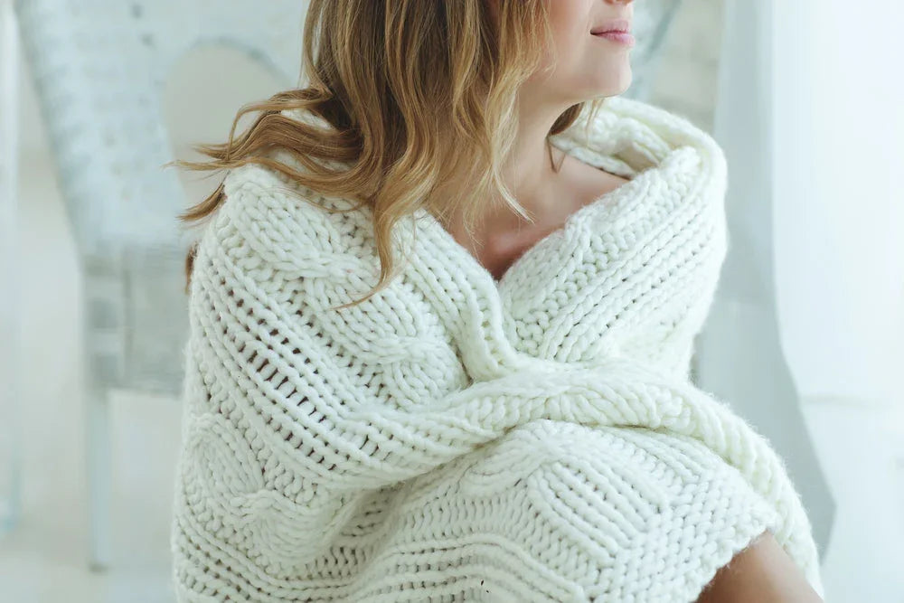 Woman wrapped in a soft white knit blanket, cozy in a bright allergy-free home setting