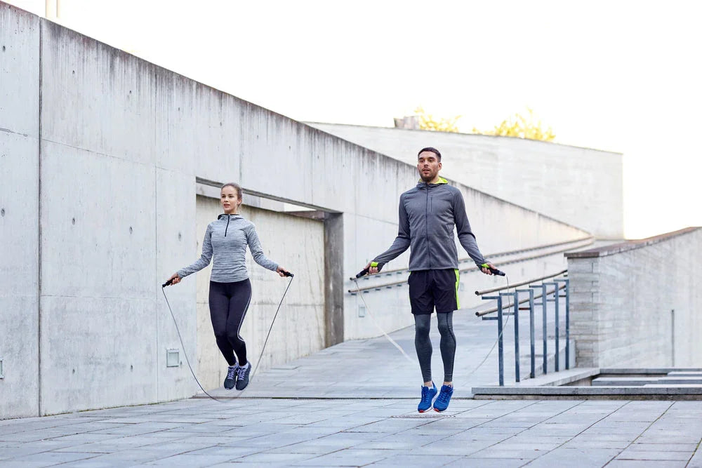 Two people in athletic wear jump roping outdoors on concrete, allergy-friendly activewear.