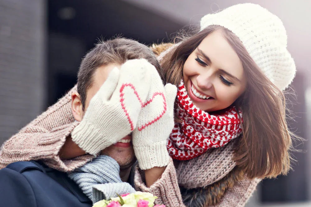 Smiling woman in allergy-free knit hat and gloves covers man's eyes outdoors