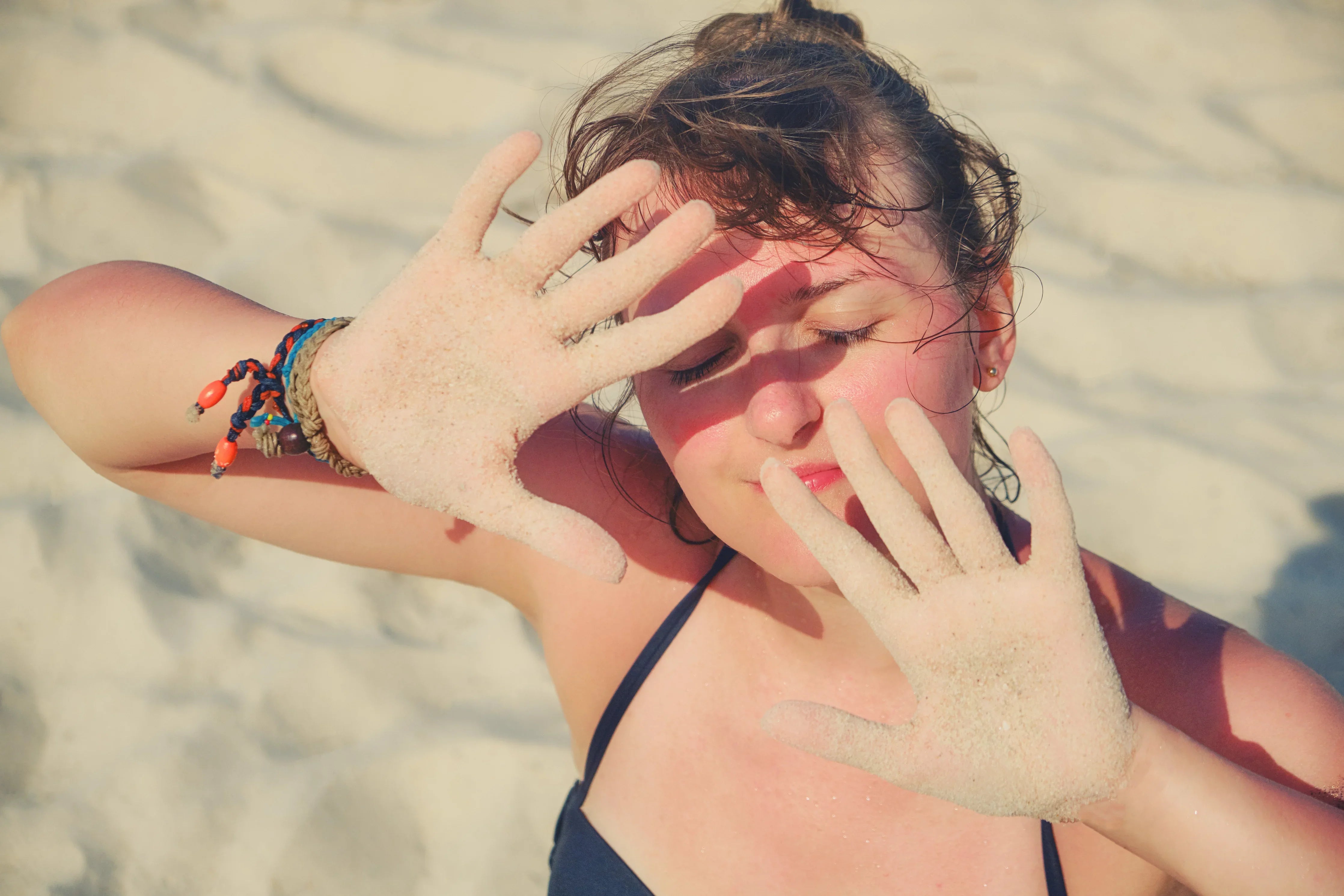 Woman on sandy beach shielding face from sun, wearing allergy-free summer apparel