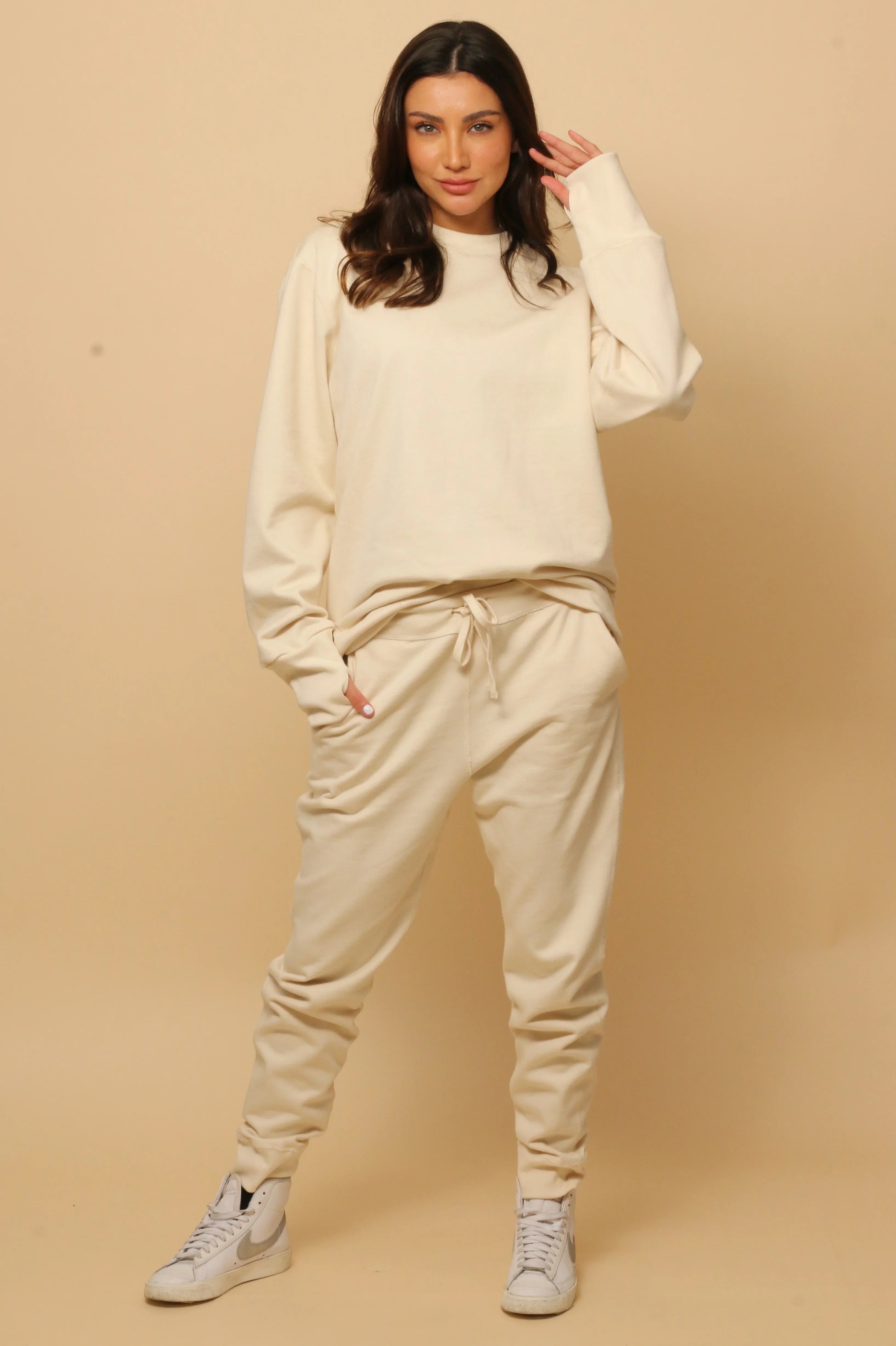 Woman wearing beige organic cotton sweatshirt and jogger pants, standing in studio