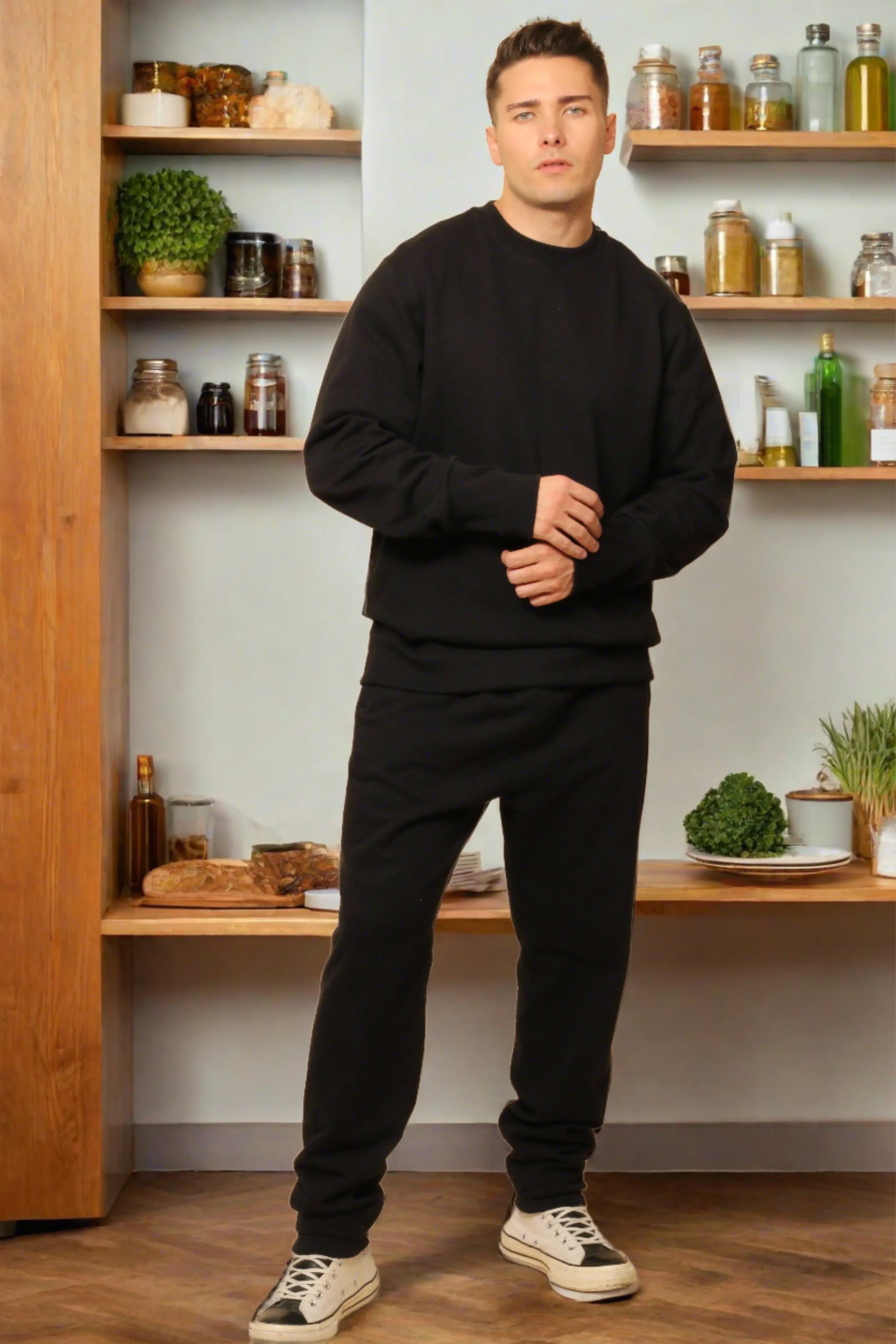 Man wearing black organic cotton sweatshirt and pants, standing in cozy kitchen setting