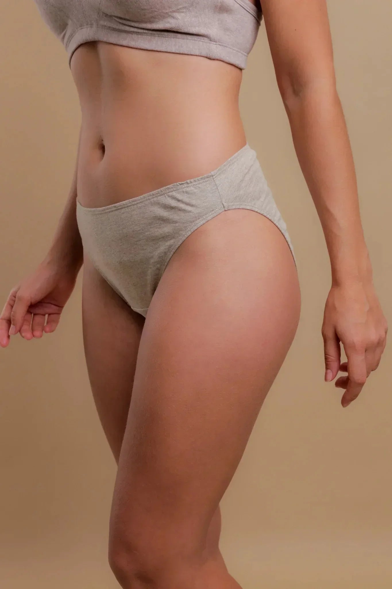 Woman wearing light grey organic cotton underwear set, side view, on beige background