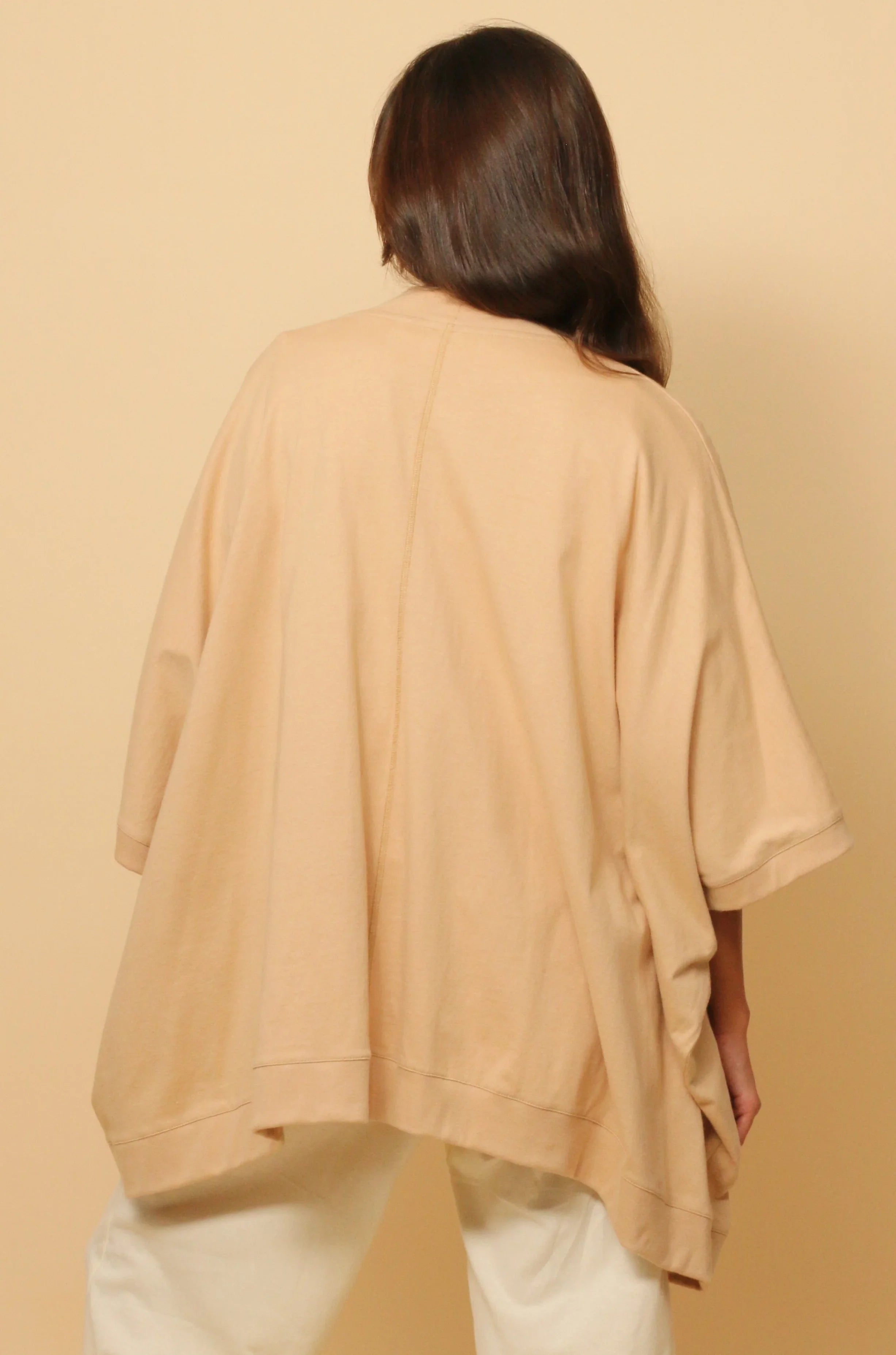 Back view of woman wearing loose beige organic cotton top with elbow sleeves